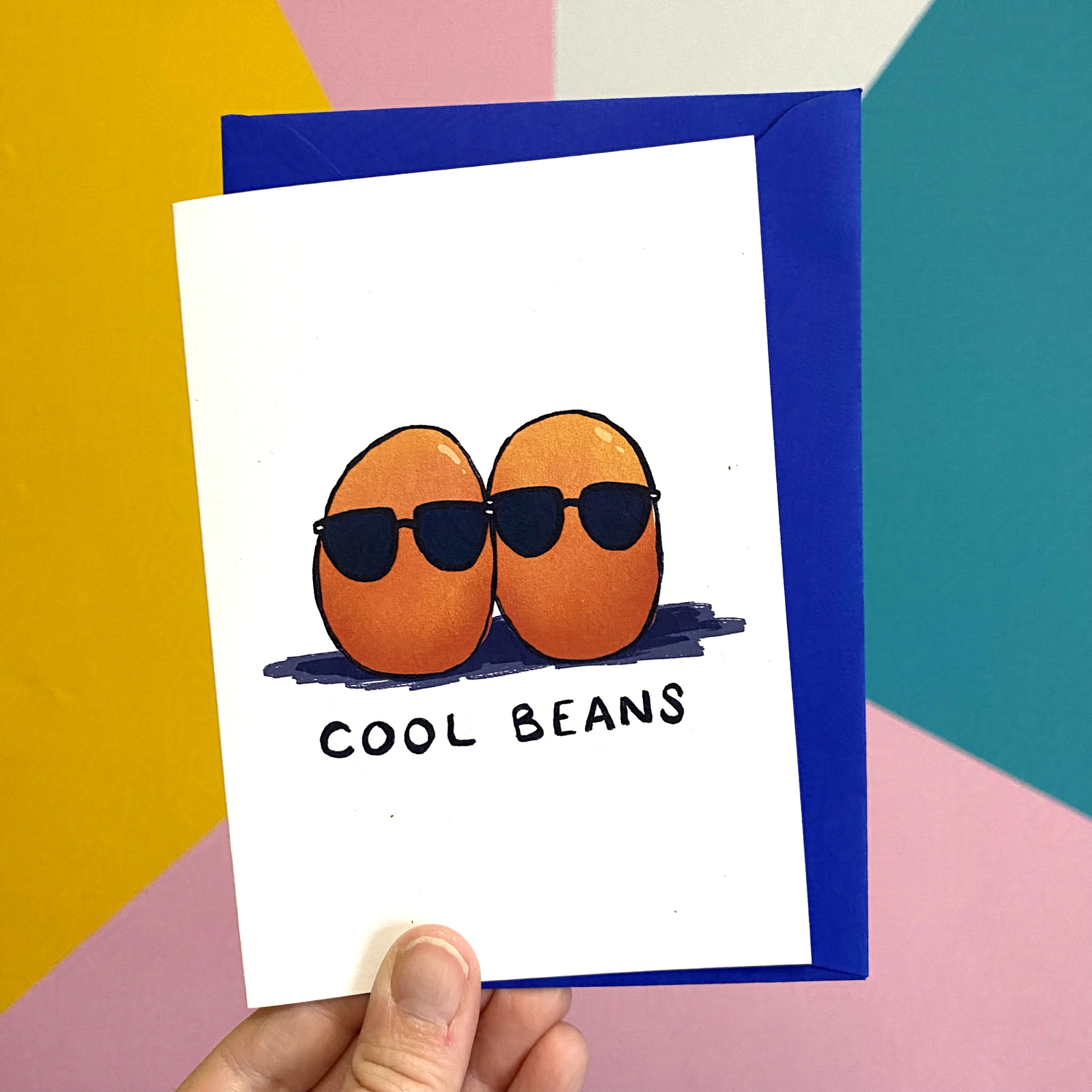 A hand holds a card featuring an illustration of a black and white cat wearing shades and clicking its fingers. Underneath are the words 'Cool Cat'