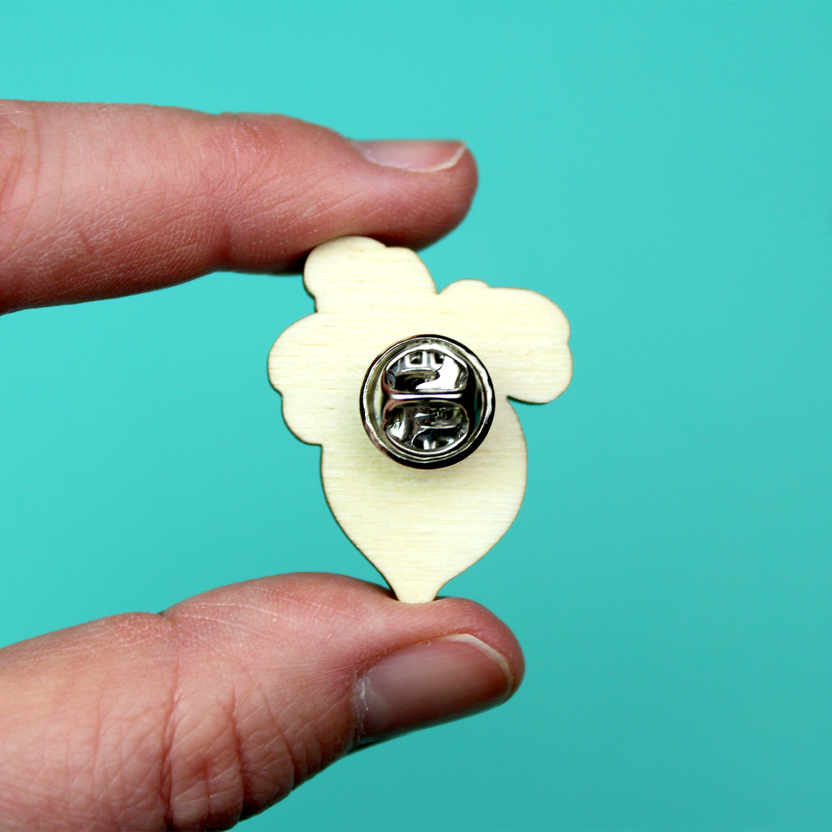 A hand holds up the back of the wooden pin to show the metal butterly clasp.