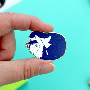A wooden pin badge is shown that has the illustrated picture of a chute blue and white cat. the cat is sleeping all curled up. it has a chin dot.