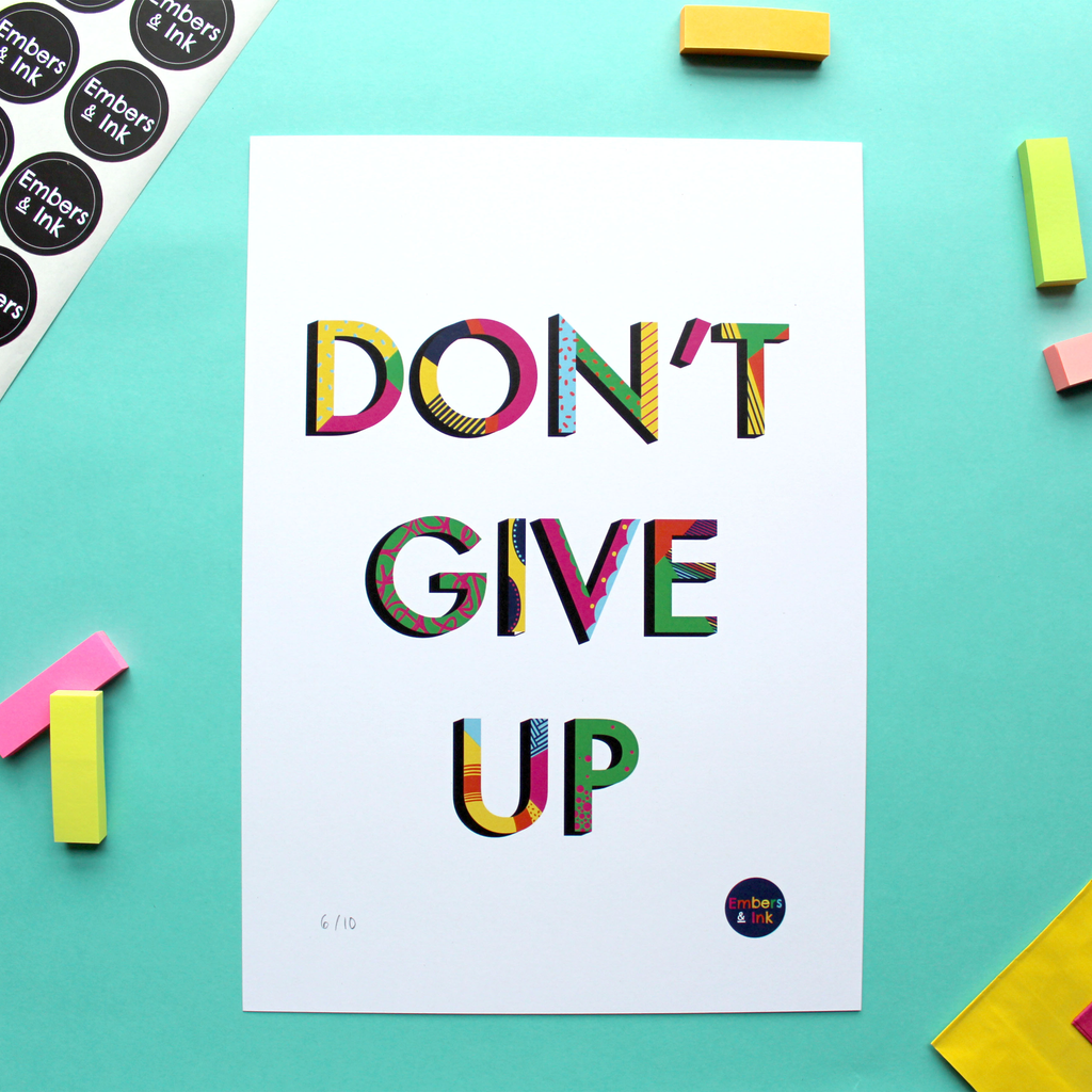 An art print in portrait orientation features the coloured and patterned words Don't Give Up against a white background.