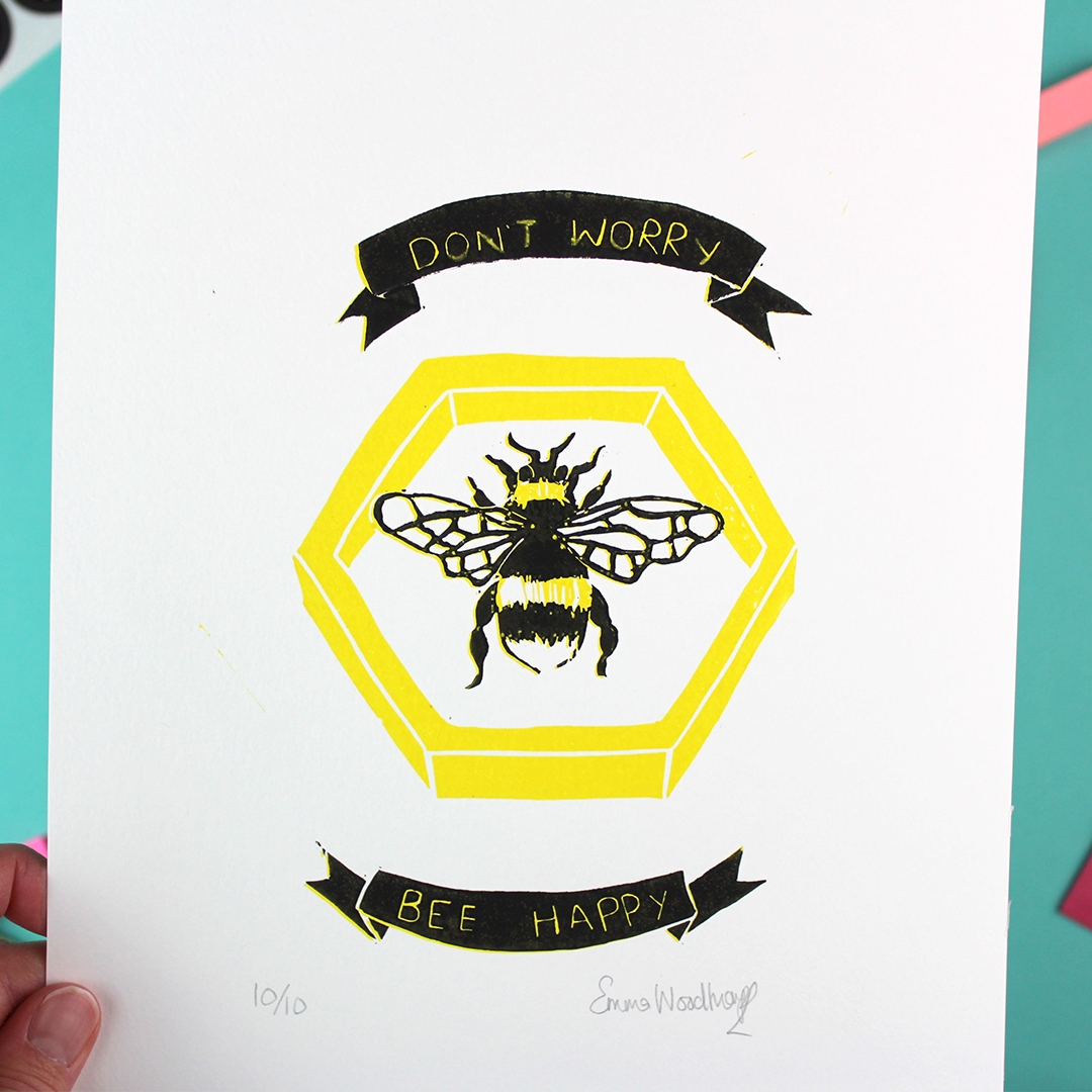 A hand holds up the don't Worry Bee happy art, showing that it is signed and numbered