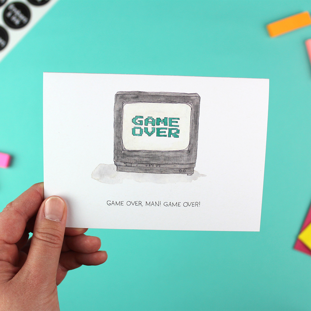 A hand holds up a landscape orientated greetings card with an illustrated image of a tv showing a 'game over' computer game end-screen. Underneath are the words 'game over, man! game over!'