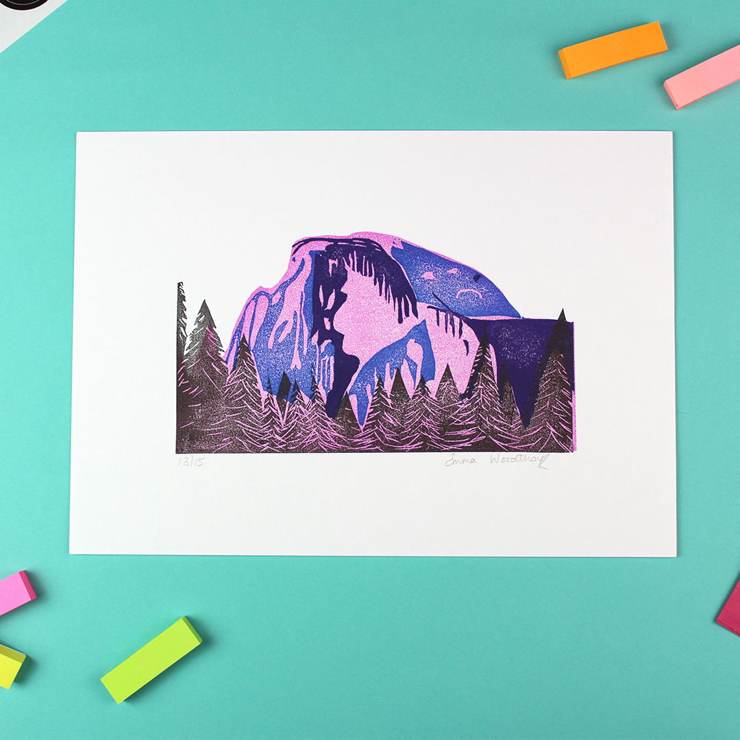 a landscape orientated piece of art is shown. it is A4 size and contains a printed image of Half Dome, make from a lino cut stamp. It is pink, blue, purple and black.