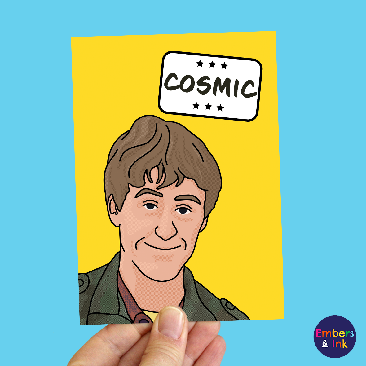 a hand holds a yellow card with an illustration of Rodney from a well known TV program underneath the word 'Cosmic' in a white box