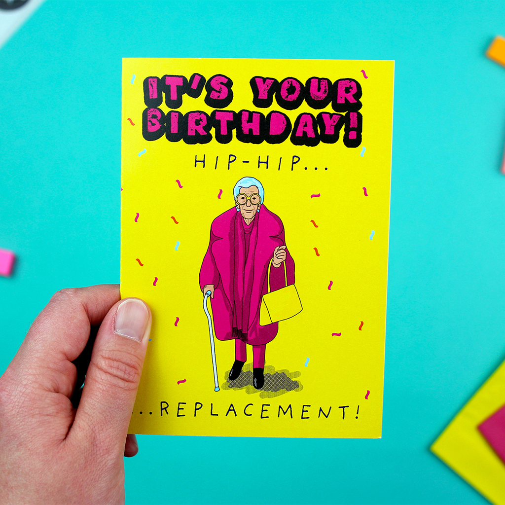 A hand holds a brght and funky greetings card showing a cool older person dressed in pink with a yellow handbag, next to the words 'It's your birthday! Hip-hip...replacement!' The background is yellow and the person is surrounded with confetti.