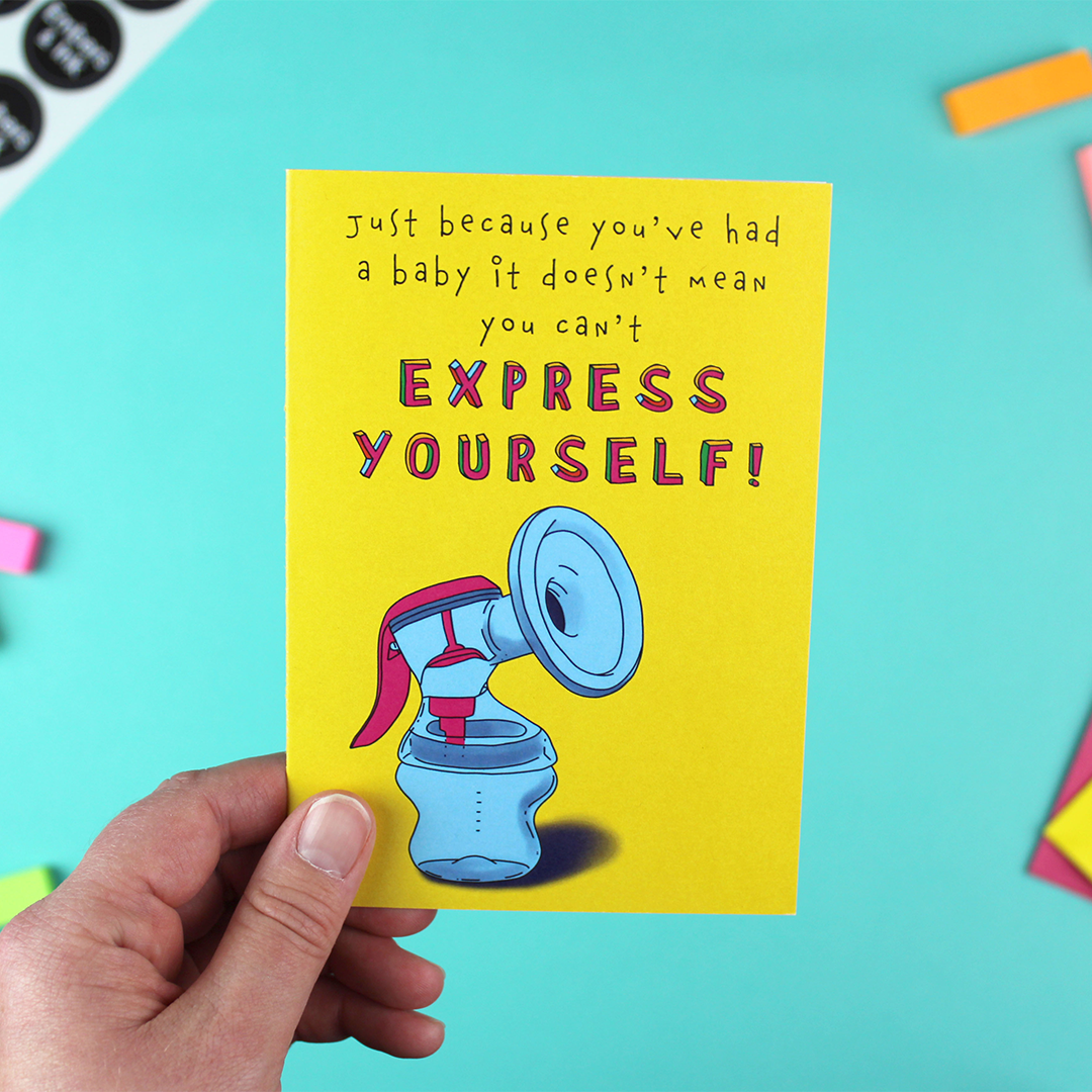 A hand holds a bright and colourful greetings card aimed at new parents. it shows an illustration of a breast pump for expressing milk, under the words: 'Just because you've had a baby it doesn't mean you can't Express Yourself'.