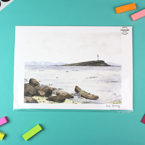 The image shows a landscape orientated print of a watercolour seascape that shows a lighthouse in the mid-distance on an island. In the distance are purple mountains.