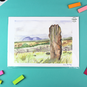 This image shows a landscape orientated print of a watercolour landscape which features a standing stone in the foreground. in the background are purple mountains.