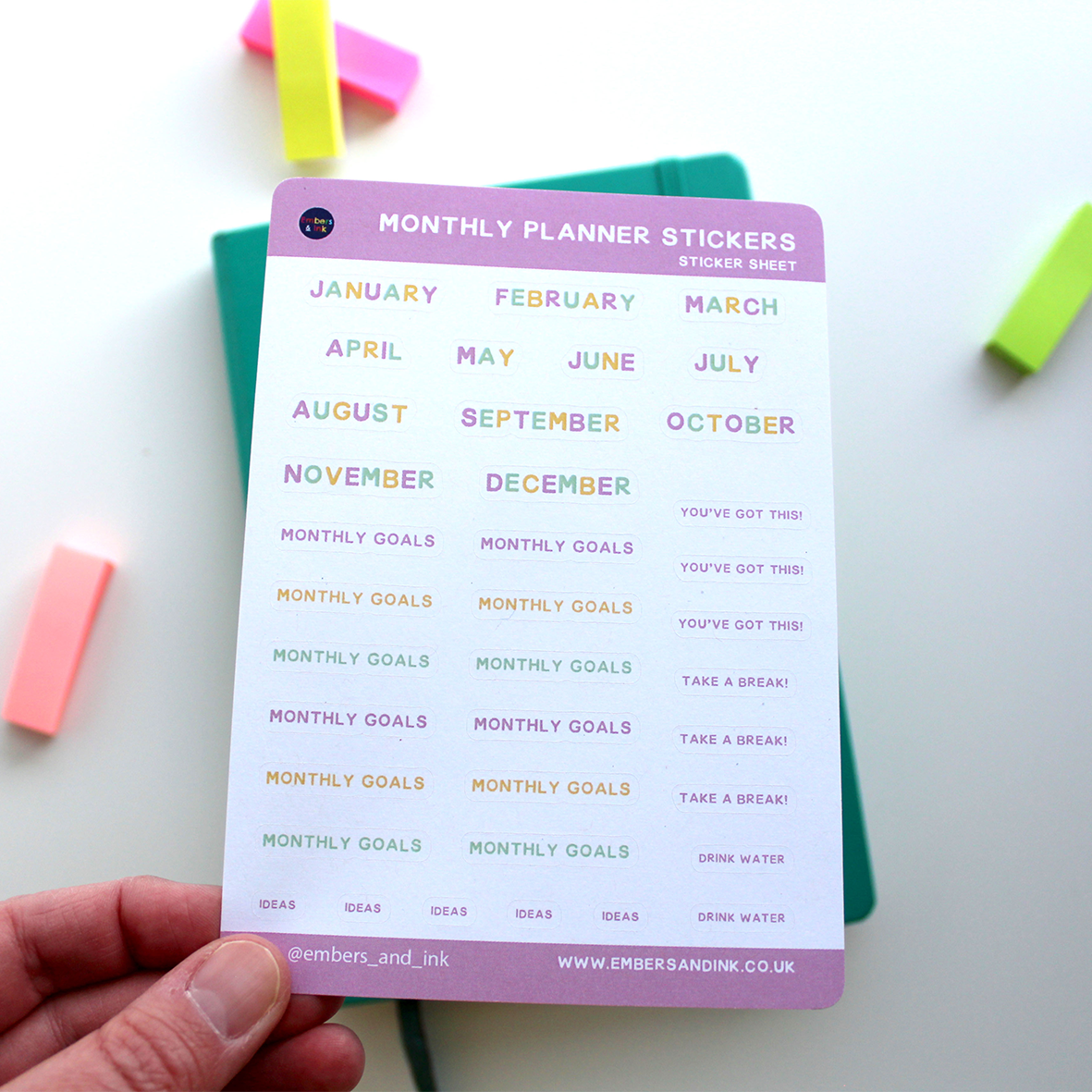 A hand holds the sticker sheet above a closed journal.