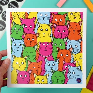 A hand holds the colourful cats poster to the camera to give an idea of size and scale. The poster measures 21cm by 21cm.