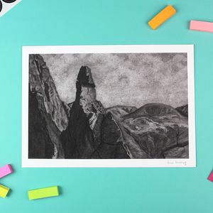 A landscape orientated print of a charcoal drawing lays on a table. The drawing is of a rock pinnacle in the Lake District called Napes Needle.