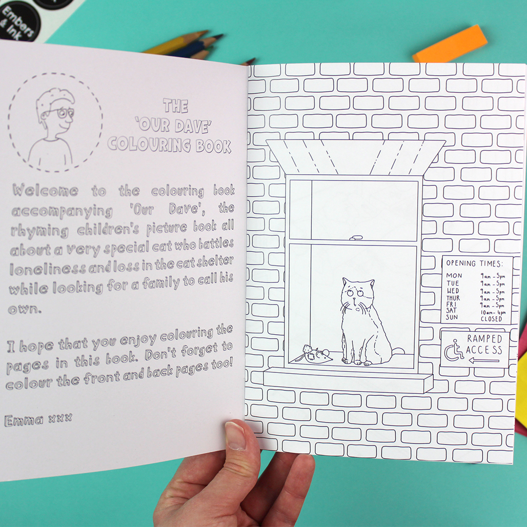 A hand holds open the colouring book to show the inside cover - which has a welcome note-  and the first page which shows a cat looking out of a window. both pages are black and white and ready to be coloured in.