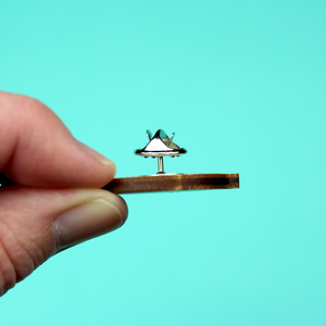 A hand holds the woden pidge on its side to show that it is approximately 3mm wide, and has a metal pin and metal butterfly clasp.