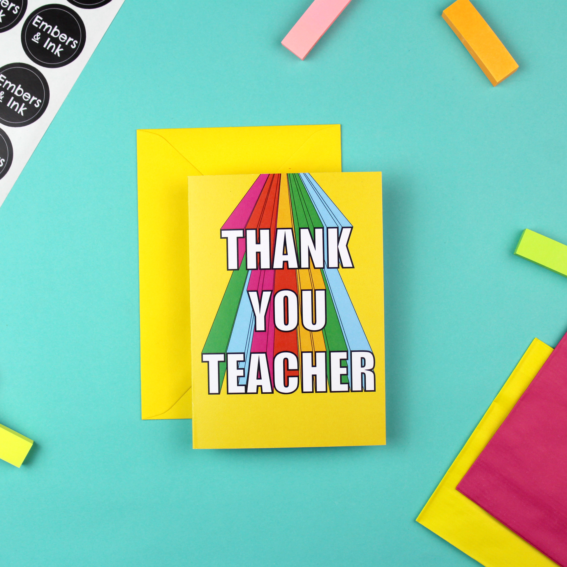 The image shows a bright and colourful Greetings Card and a yellow envelope. The card has a yellow background and rainbow coloured 3D lettering that reads Thank You Teacher.