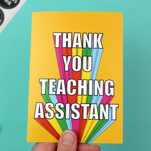 A colourful card with a yellow envelope is shown. The card is orange with rainbow block lettering that reads Thank You Teaching Assistant.
