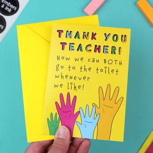 A hand holds a yellow card with a yellow envelope. The card has an illustration of four raised hands in green, pink, blue and orange. Above the hands are the words 'Thank You Teacher, now we can both go to the toilet whenever we like'.