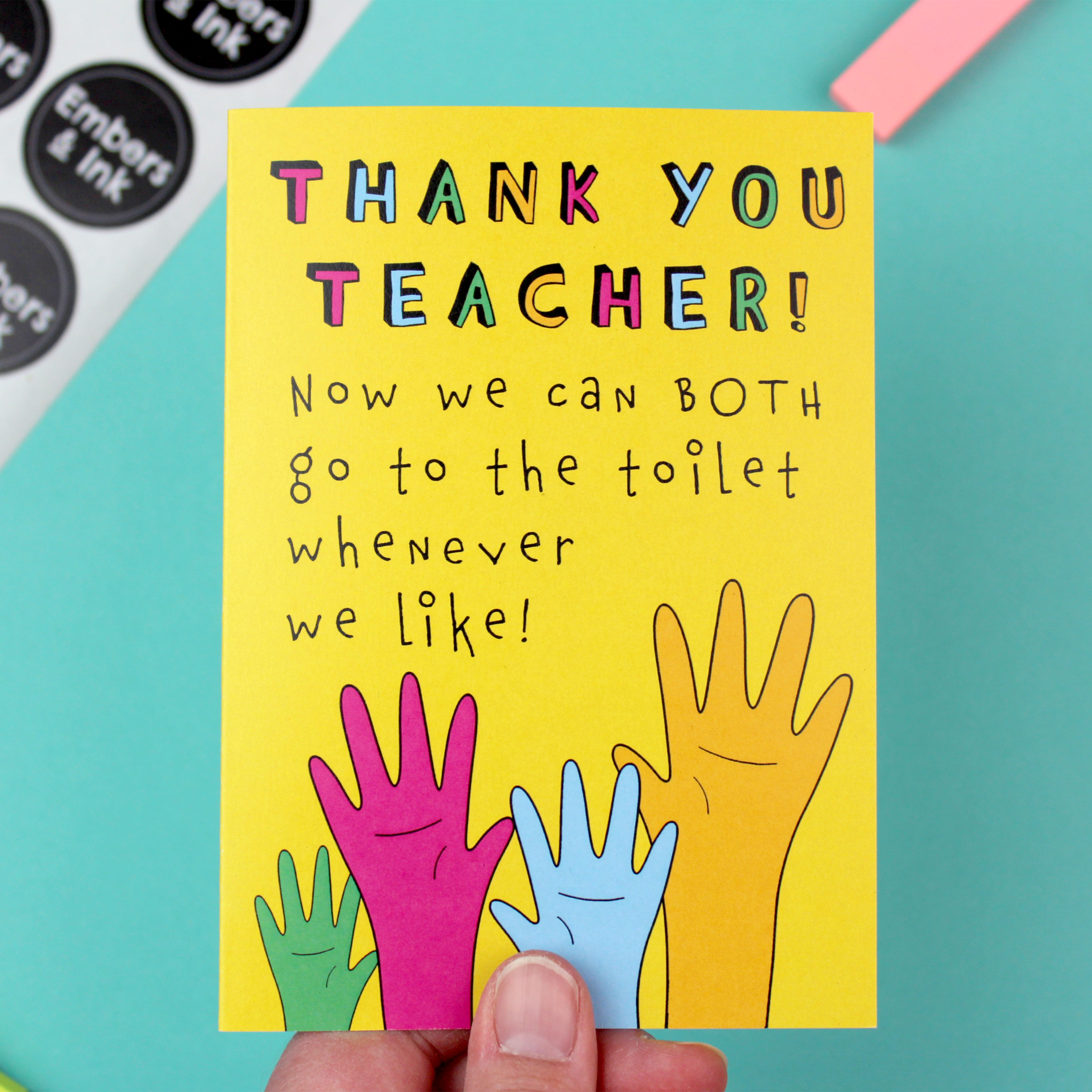 A hand holds a yellow card. The card has an illustration of four raised hands in green, pink, blue and orange. Above the hands are the words 'Thank You Teacher, now we can both go to the toilet whenever we like'.