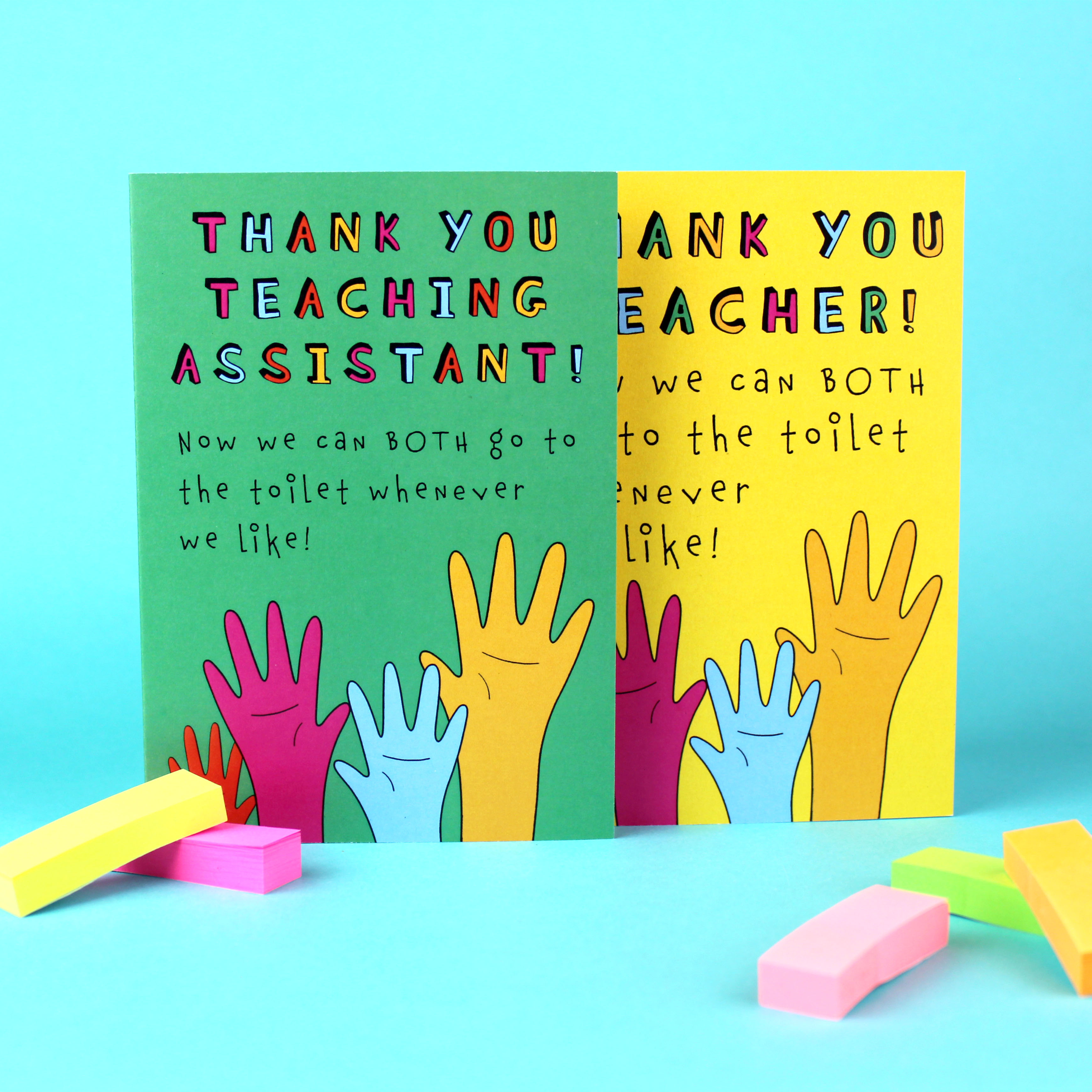 Two greetings cards are shown: one with a green background and one with a yellow background. Both have an illustration of raised hands of various colours. The yellow card reads Thank You Teacher now we can both go to the toilet whenever we like!. The green card says the same, but for a Teaching Assistant.