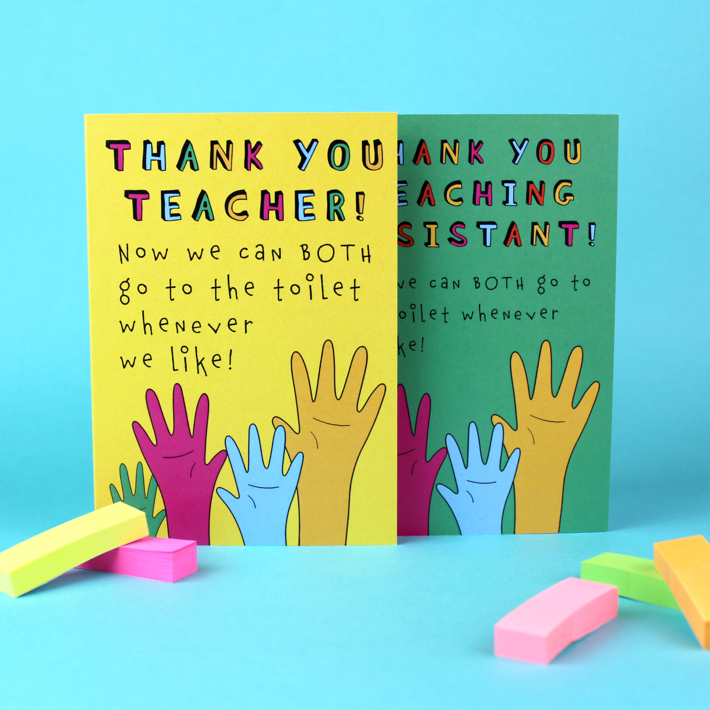 Two greetings cards are shown: one with a green background and one with a yellow background. Both have an illustration of raised hands of various colours. The yellow card reads Thank You Teacher now we can both go to the toilet whenever we like!. The green card says the same, but for a Teaching Assistant.