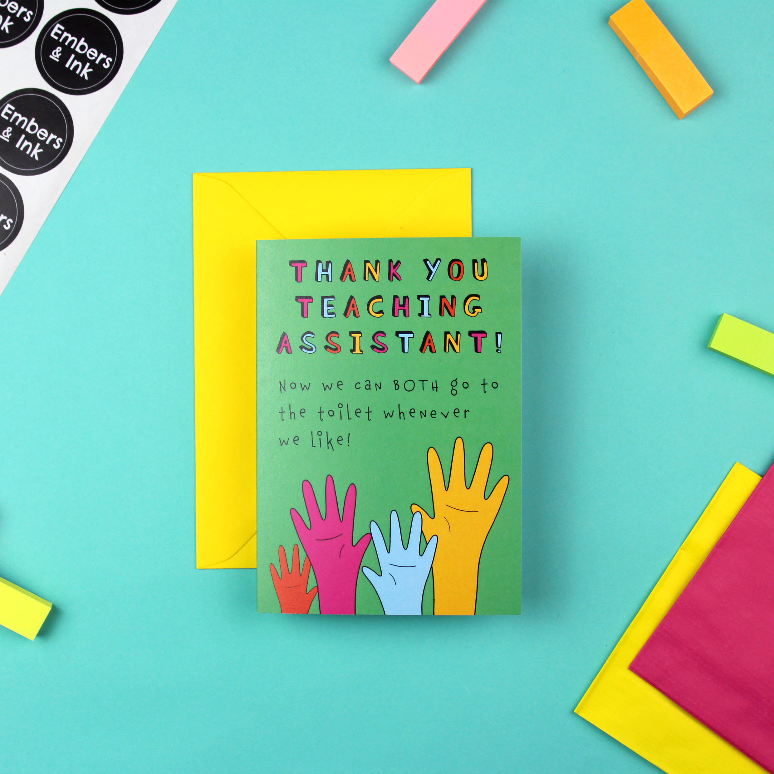 The image shows a brightly coloured card and a yellow envelope. The card is green an features an illustration of four raised hands in orange pink blue and yellow. Above it are the words 'Thank you teaching assistant! Now we can both go to the toilet whenever we like!'