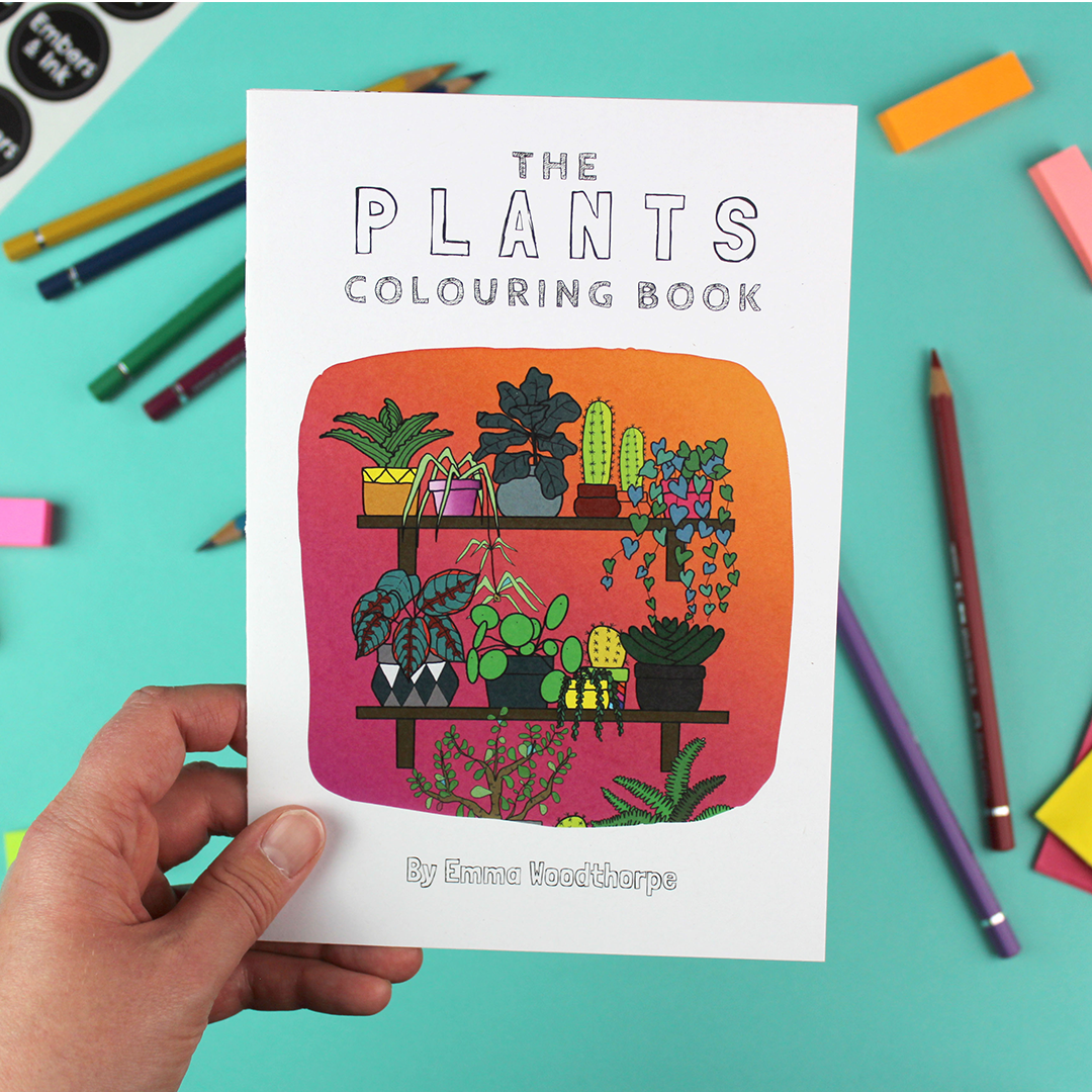 A hand holds up the plants colouring book that has a brightly coloured ilustration of two shelves full of house plants
