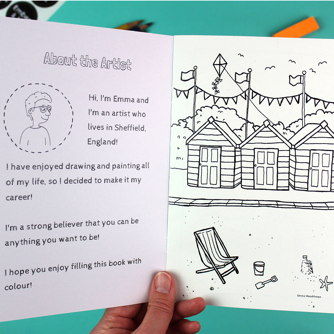 A hand holds open the colouring book to show a welcome message on the inside cover and the first page which shows the beach hut scene from the front cover.