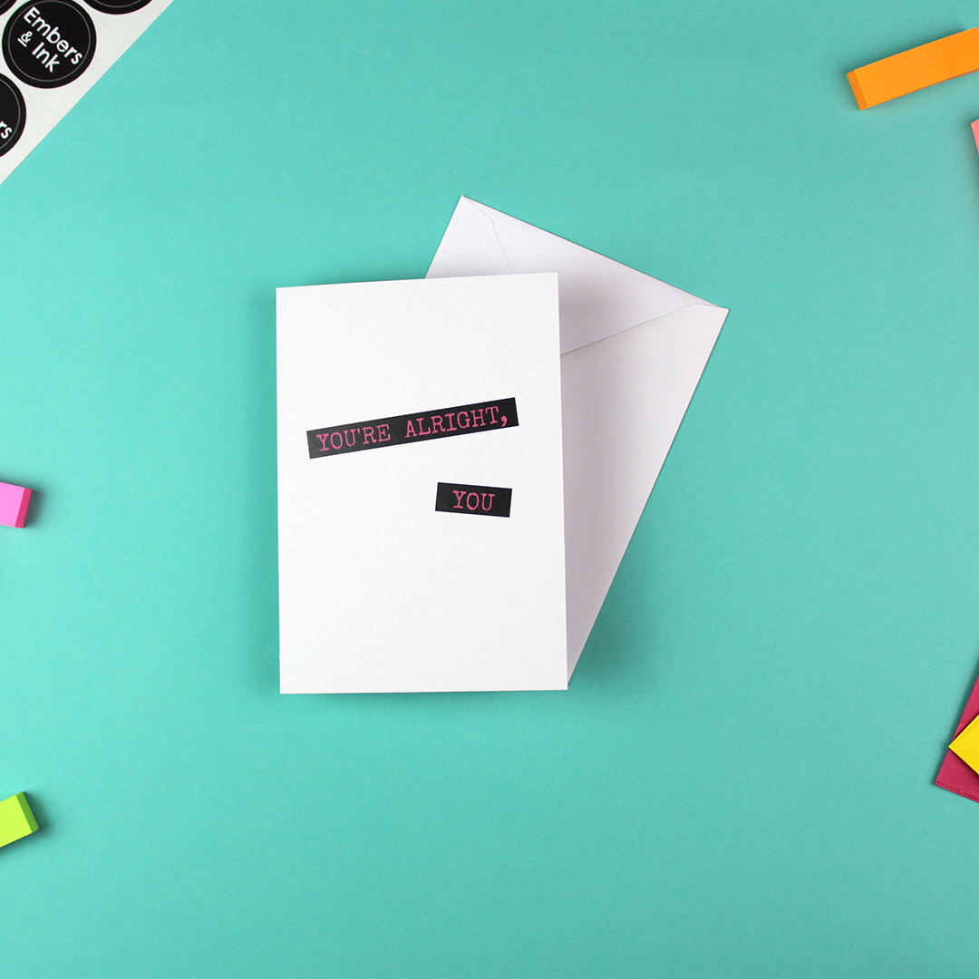 A withe card with pink writing on a black background shows the words 'you're alright, you' in a font that looks like a dymo-label writer.