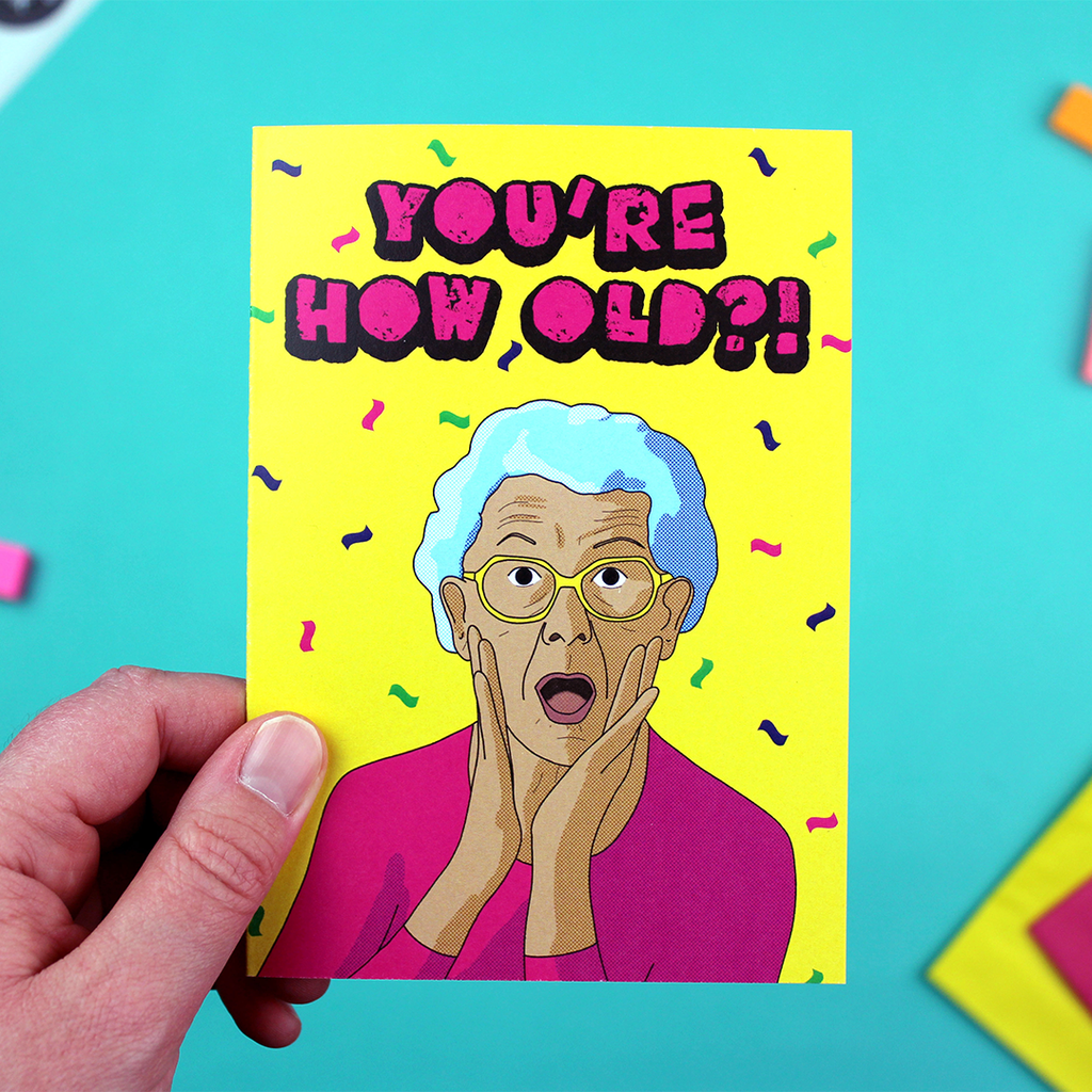 A hand holds a bright A6 card, with an illustration of an older person looking shocked under the words 'You're How Old?"' in all caps.