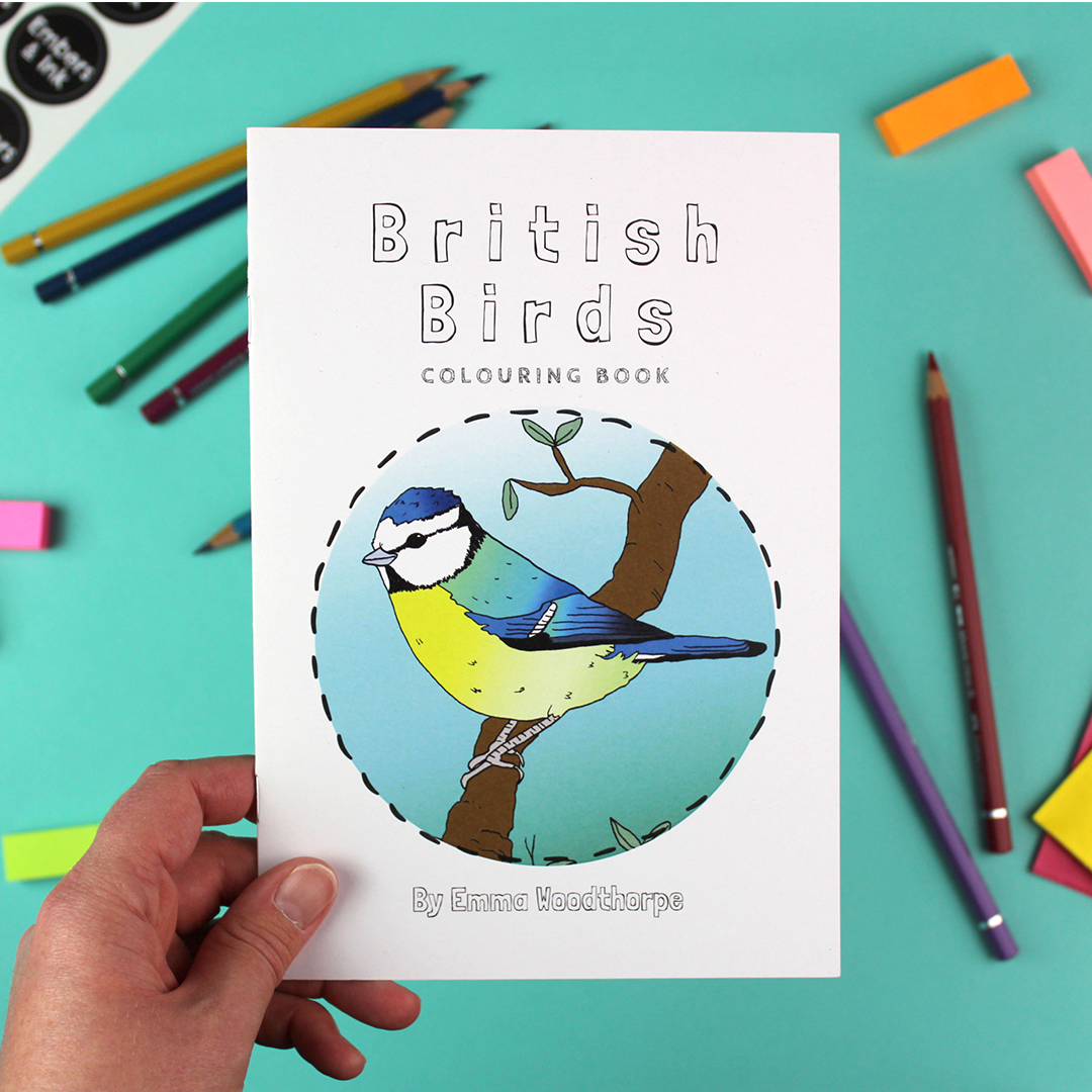 A hand holds the British Birds Colouring book. The front cover has an illustration of a colourful blue tit.