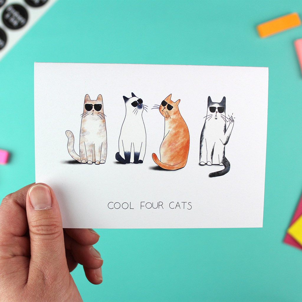 A hand holds a landscape orientated greetings card that contains an illustration of four cats, all wearing shades, with the cat on the end also clicking its fingers. Underneath are the words 'cool four cats'.