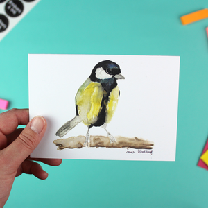 A hand holds up a landscape-orientated A6 greetings card featuring a watercolour image of a Great Tit Bird.