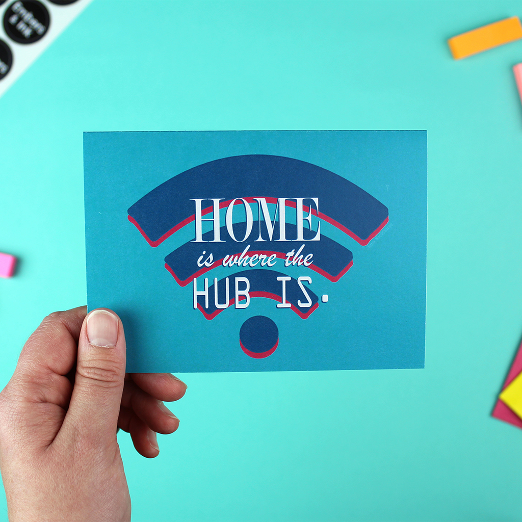 A hand holds up a landscape orientated greetings card with a teal (greeny blue)background, with a blue wifi logo on it. Over that are the words 'home is where the hub is'.