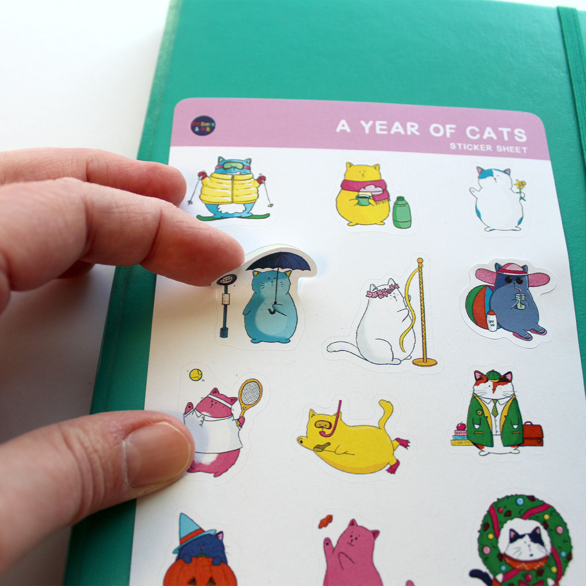 A hand is shown easily peeling one of the cat stickers from the sheet.