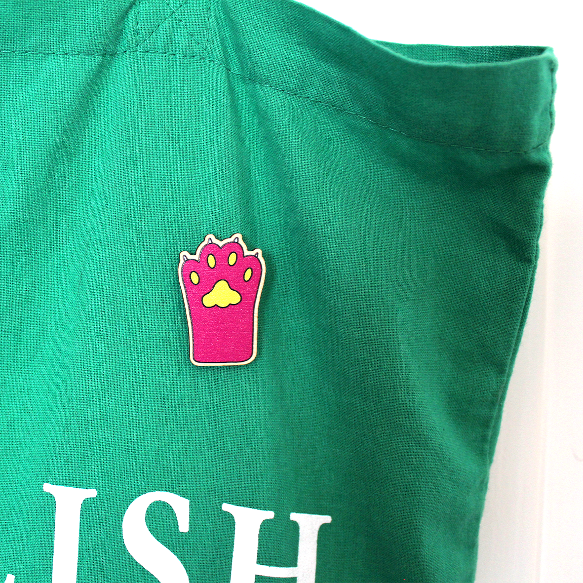 A close up of the pink paw pin badge on the green cotton tote bag