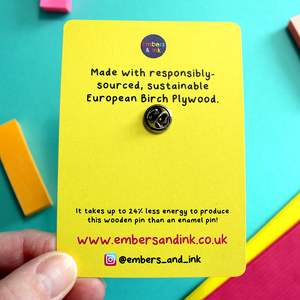 the rear of the cardboard display backer is shown. it reads: Made with responsibly sourced sustainable European birch plywood. It takes up to 24% less energy to produce this wooden pin than and enamel pin! www.embersandink.co.uk. Instagram @embers_and_ink