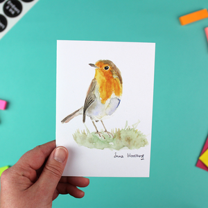A hand holds a portrait-orientated greetings card featuring a watercolour image of a robin.