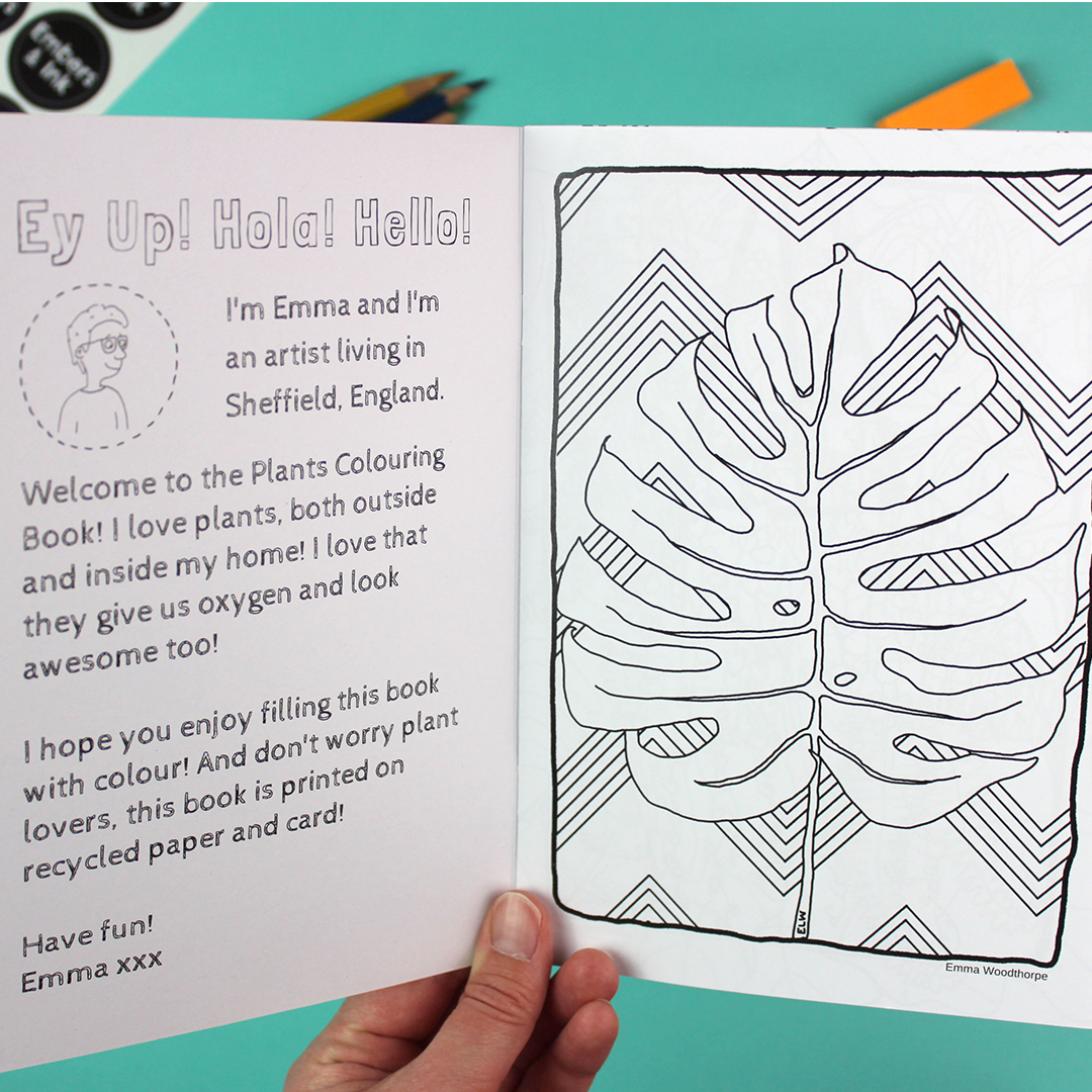 A hand holds open the colouring book to show the inside cover and the first page. both are black and white and colour-in-able