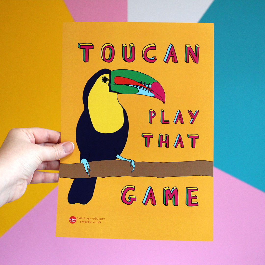 A hand holds a portrait orientated otange poster with an illustration of a toucan bird. Around it are the words Toucan Play That Game in colourful Font.