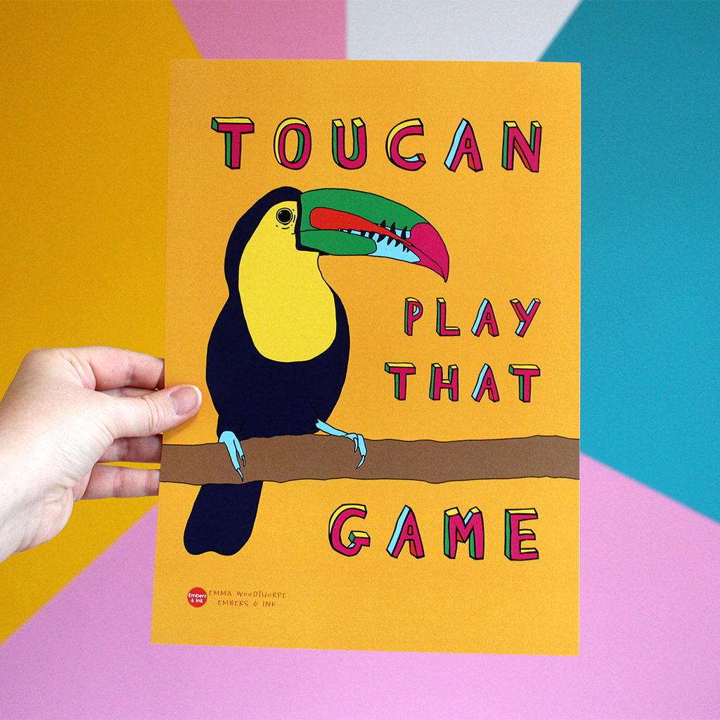 A hand holds a portrait orientated otange poster with an illustration of a toucan bird. Around it are the words Toucan Play That Game in colourful Font.