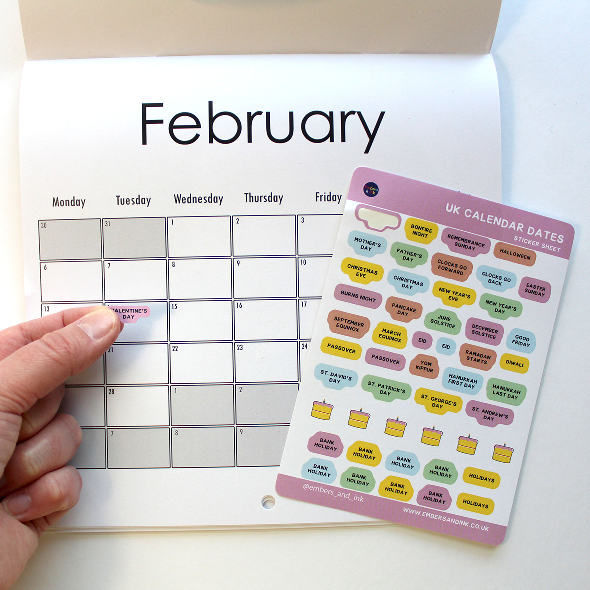 A hand is shown adding the Valentine's Day sticker from the sticker sheet, onto a calendar on February 14th