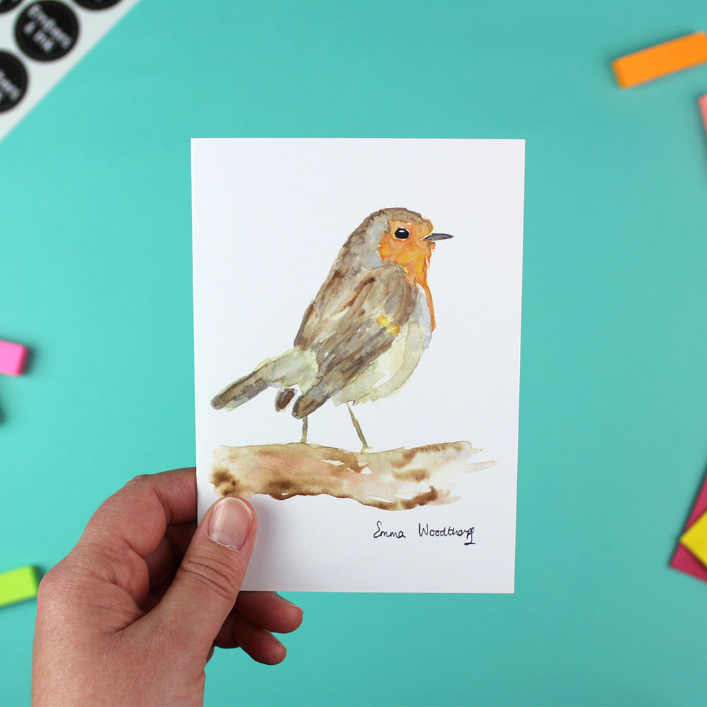 A hand holds a portrait-orientated greetings card taht features a watercolour image of a robin.