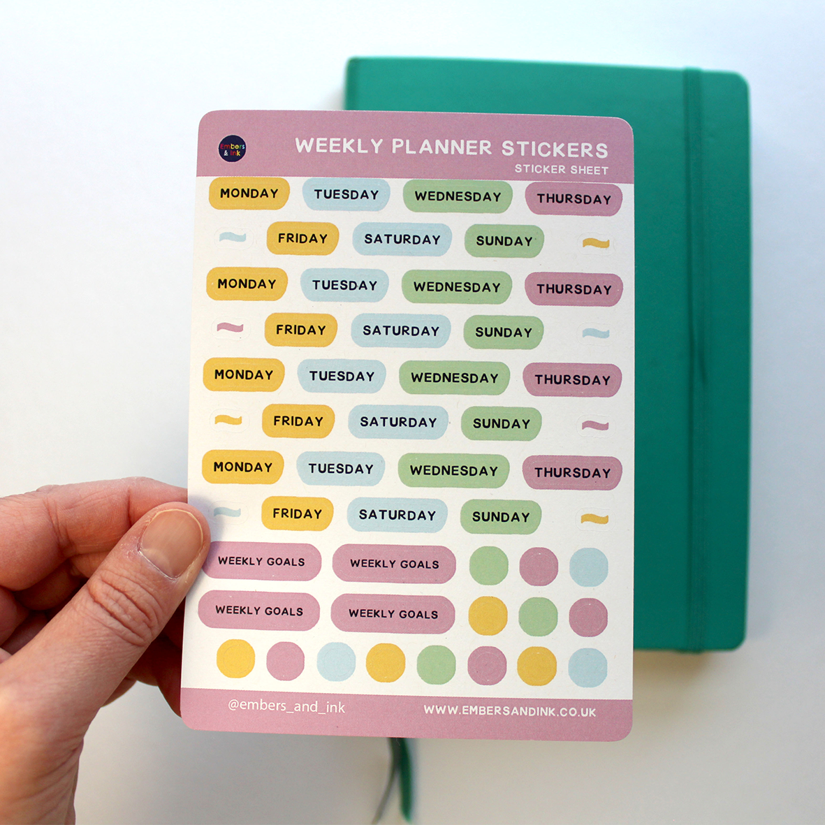 A hand holds the sticker sheet above a green journal.