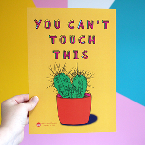 a hand holds a brightly coloure, portrait orientated poster. it is orange with pink yellow green and blue writing that reads 'you can't touch this'. Underneath is an illustration of a cactus.