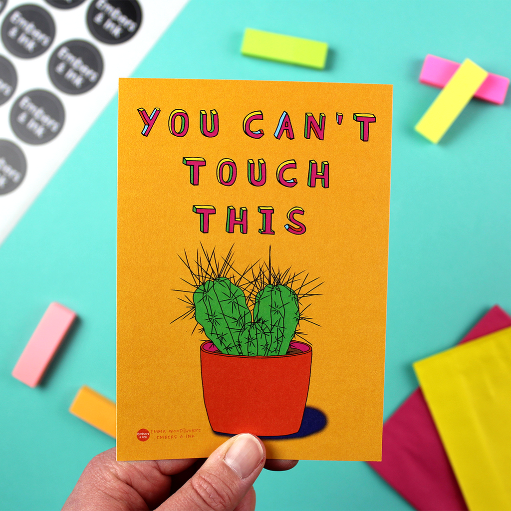 A hand holds a portrait orientated small art print with an orange background and an illustration of a cactus plant. Above it are the words You Can't Touch This